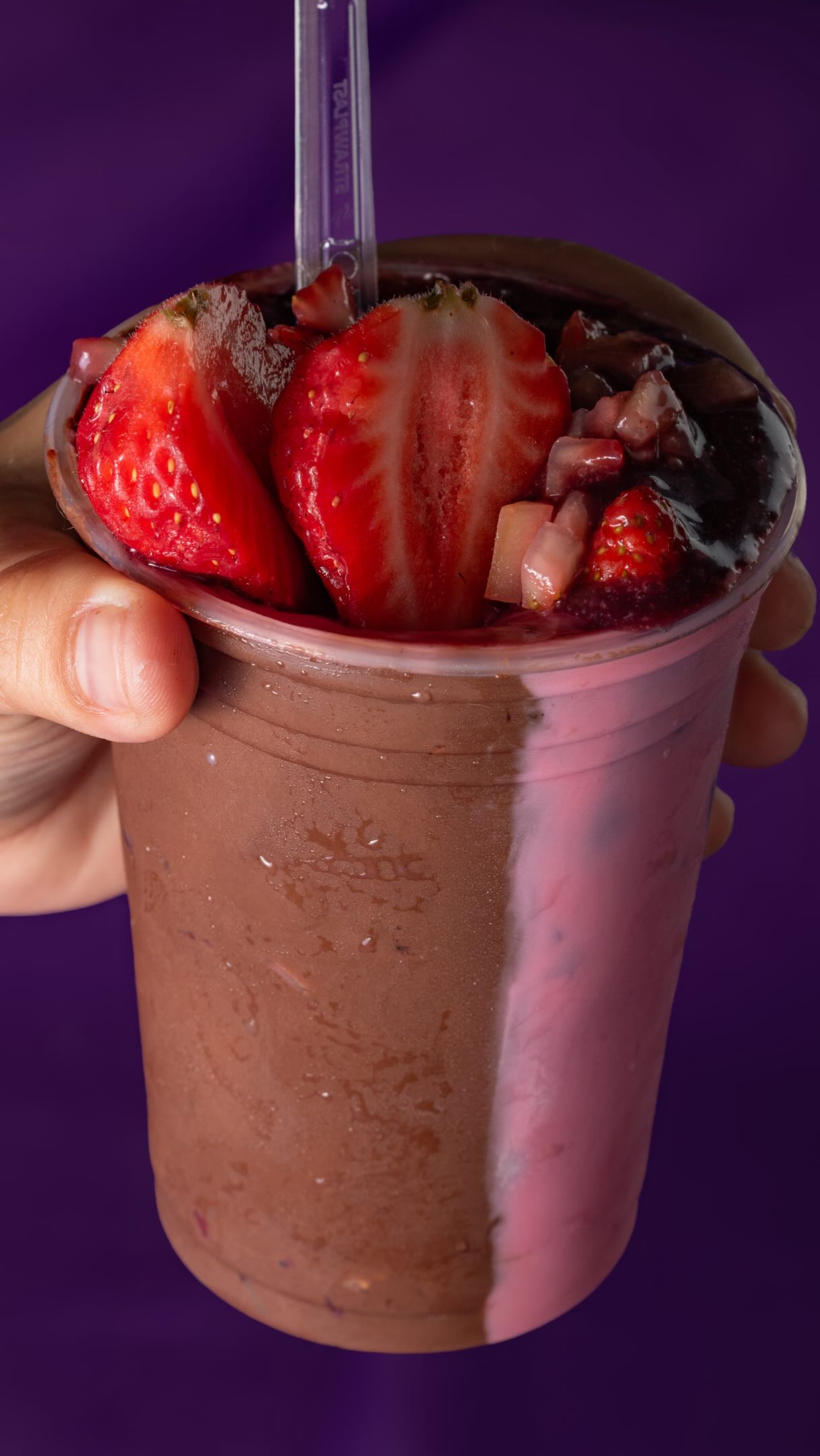 Mão segurando copo de açaí com morangos frescos